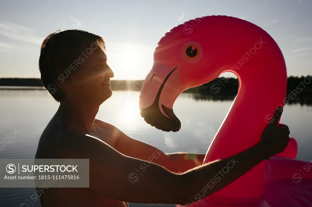 Young man with flamingo pool float at sunset