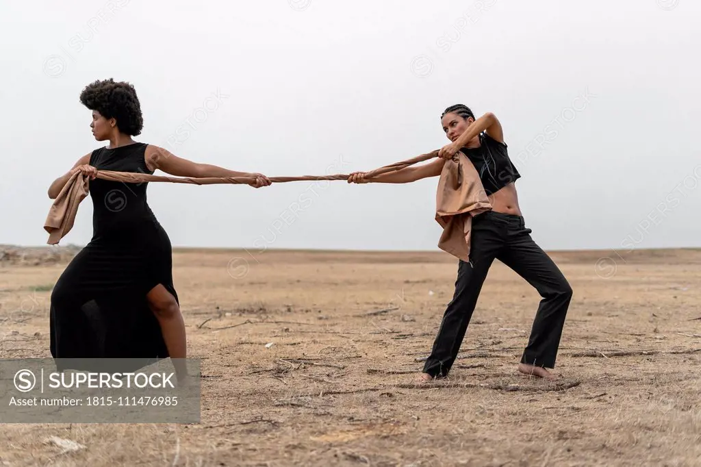 Two women pulling a cloth in bleak landscape