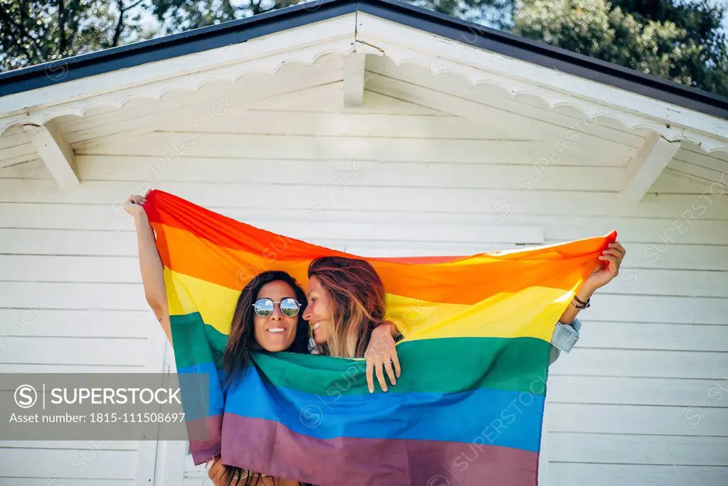 Two smiling women holding up a rainbow flag