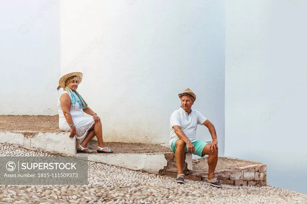 Senior tourist couple sitting on steps in a village, El Roc de Sant Gaieta, Spain