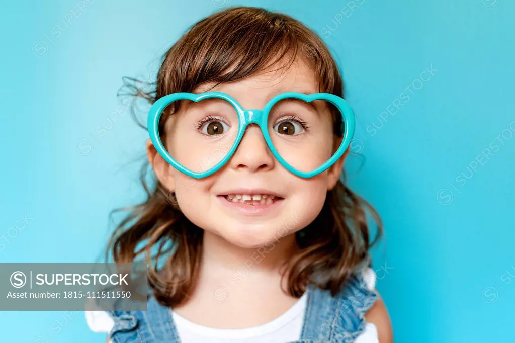 Portrait of cute little girl with heart shaped glasses on blue background