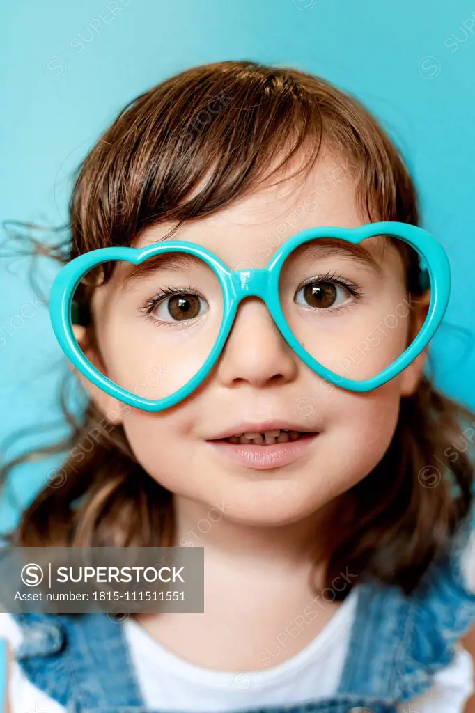 Portrait of cute little girl with heart shaped glasses on blue background