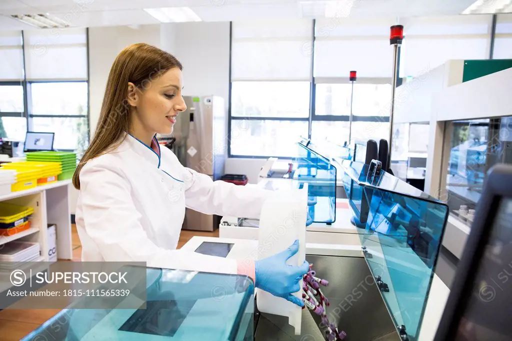 Side view of young woman in lab coat pouring vials of blood samples into refrigerator while working in research lab