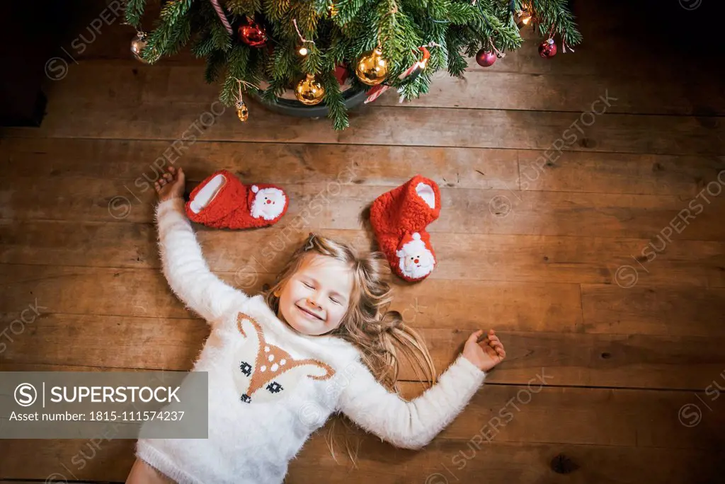 Smiling girl with closed eyes lying under the Christmas tree