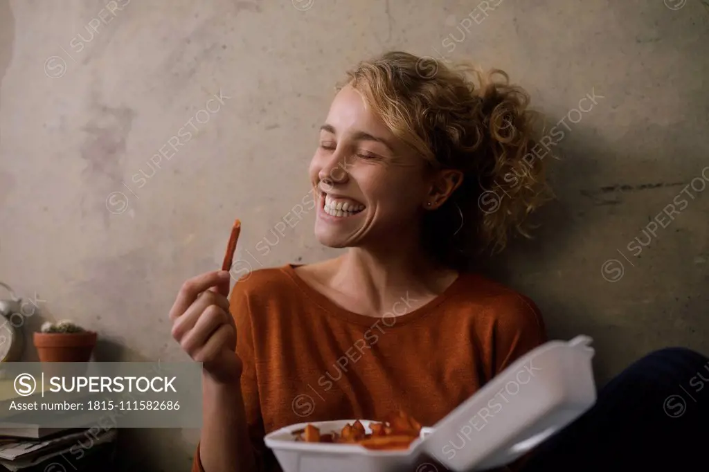 Portrait of grinning young woman eating French Fries at home