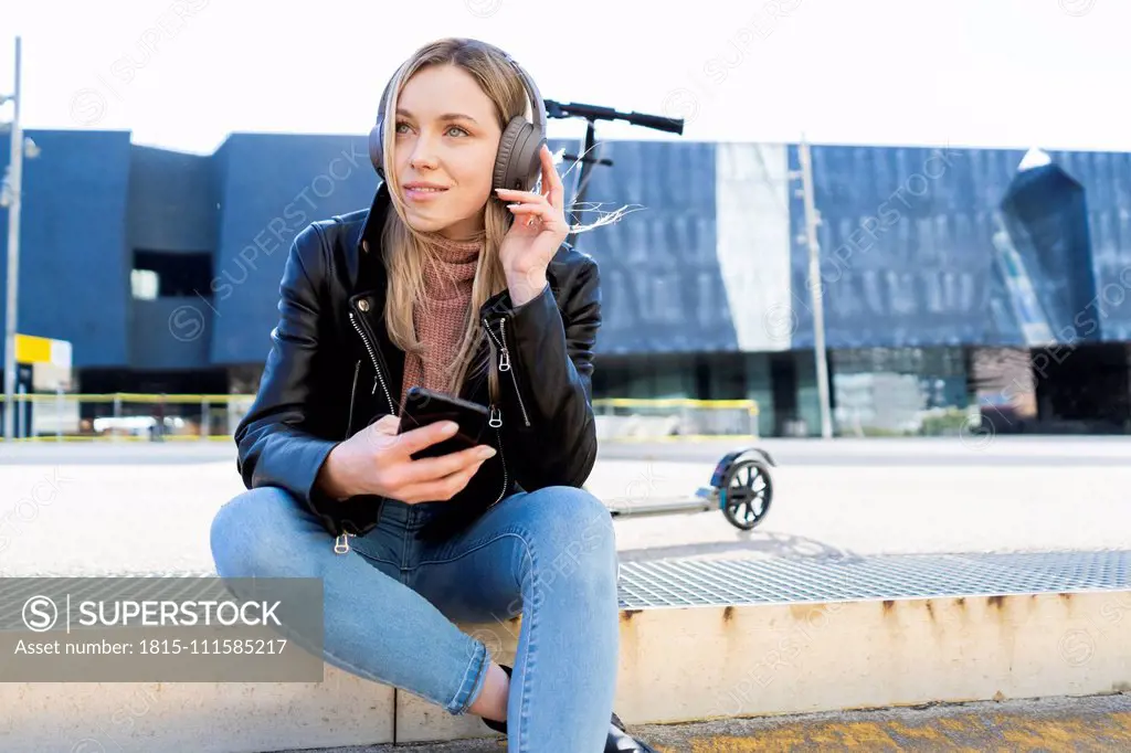 Portrait of young woman listening music with smartphone and headphones, Barcelona, Spain