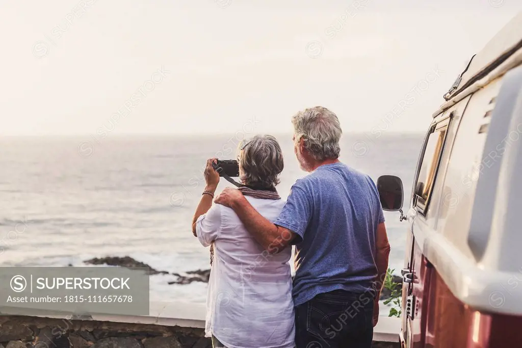 Senior couple traveling in a vintage van, taking pictures at the sea