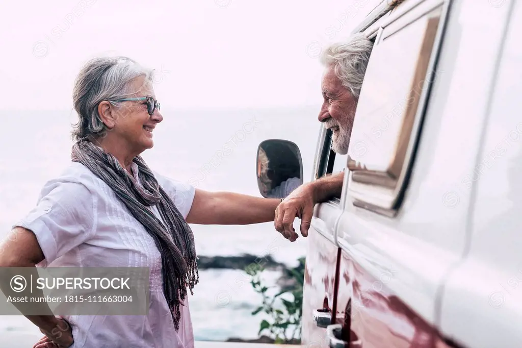 Senior couple traveling in a vintage van, taking a break at the sea, talking