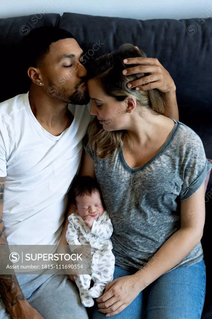 Parents cuddling with newborn baby on couch