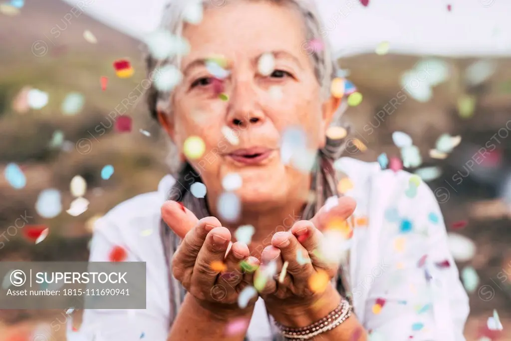 Senior woman blowing confetti outdoors