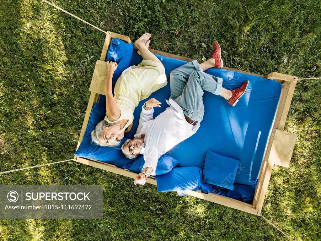 Elderly couple lying on swing bed, watching drone