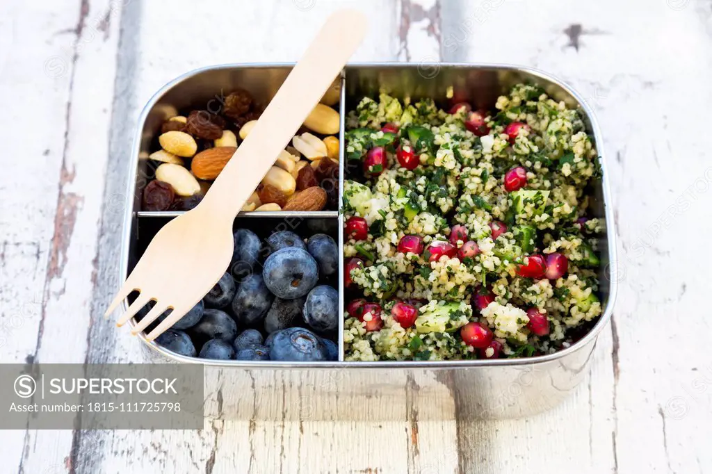 Lunchbox with bulgur herbs salad with pomegranate seeds, taboule, blueberries and trail mIx