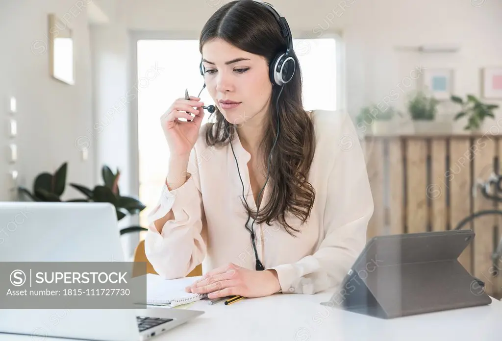 Young woman sitting at table at home wearing a headset