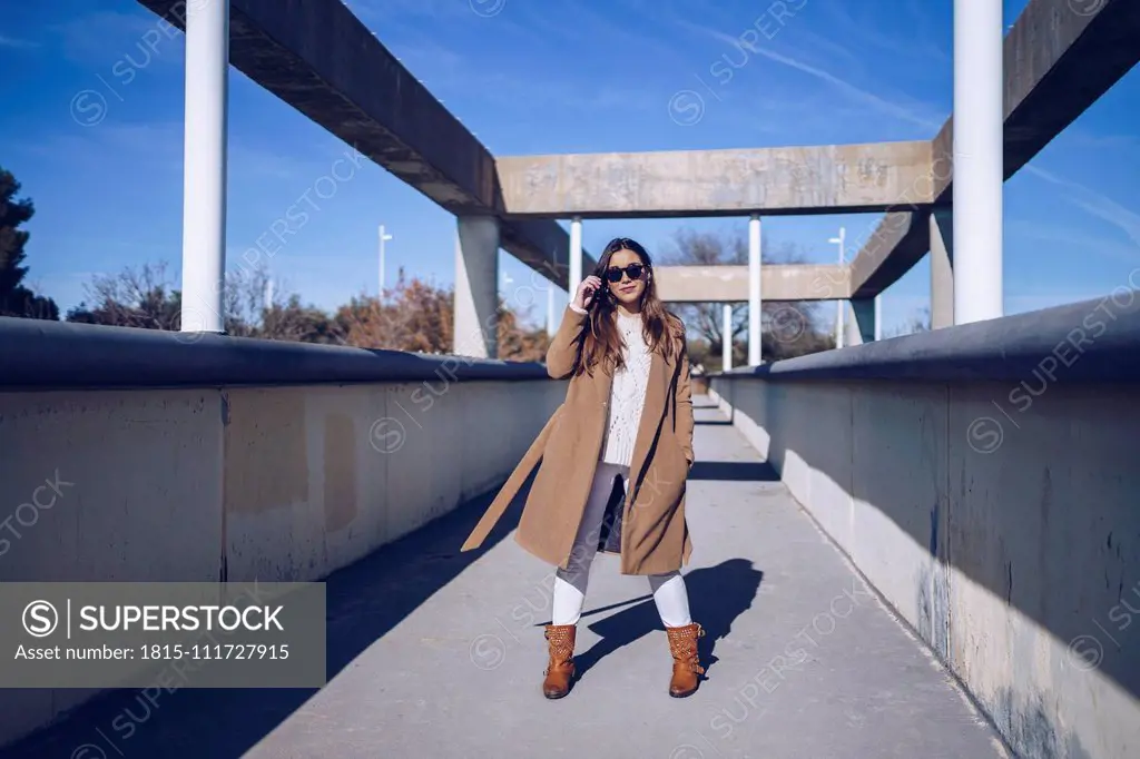 Young woman wearing coat and sunglasses standing on a bridge