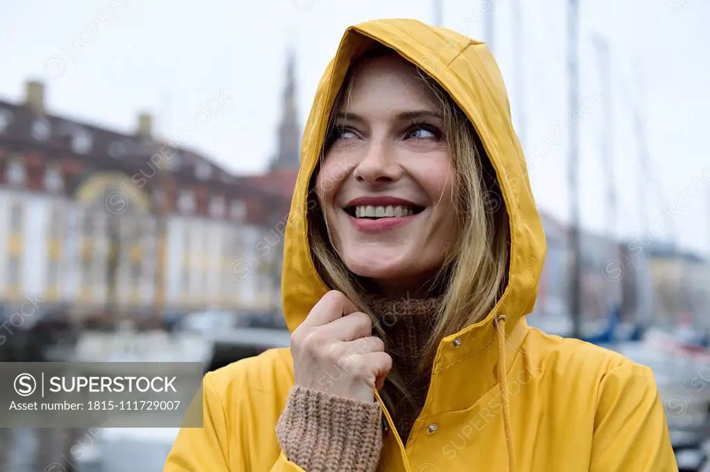 Denmark, Copenhagen, portrait of happy woman at city harbour in rainy weather