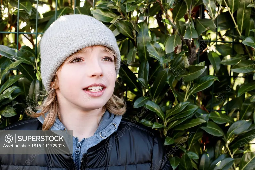 Portrait of boy wearing wooly hat at a hedge