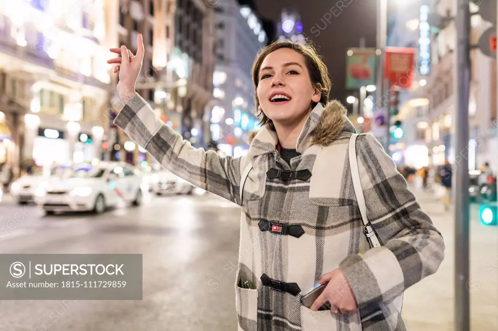 Spain, Madrid, young woman in the city at night next to Gran Via hailing a taxi