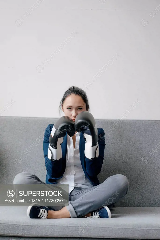 Portrait of young woman sitting on couch wearing boxing gloves