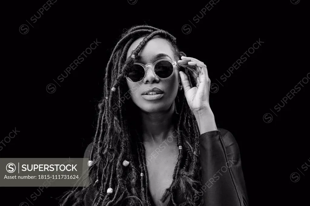 Portrait of woman with dreadlocks wearing sunglasses in front of black background