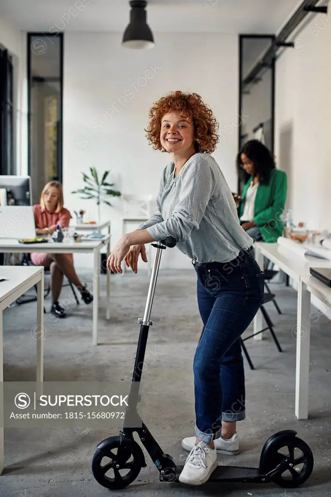 Portrait of a smiling businesswoman with kick scooter in office