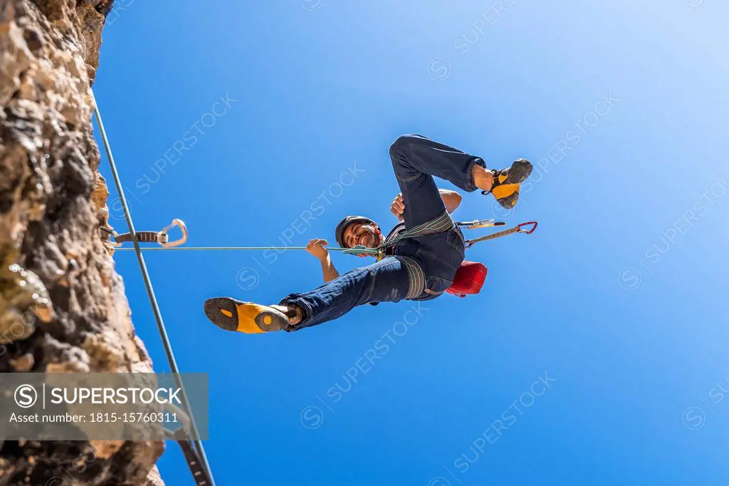 Smiling climber abseiling from rock face