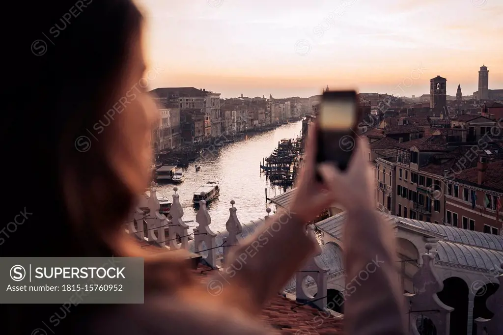 Young woman taking cell phone picture on a balcony above the city of Venice, Italy