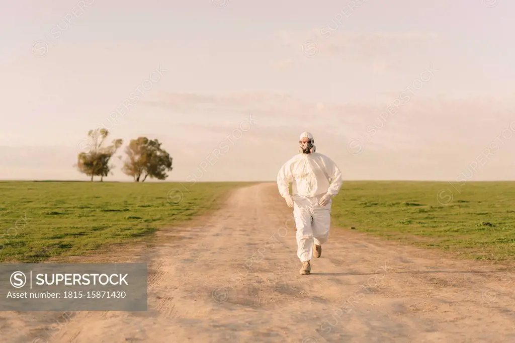 Man wearing protective suit and mask running on dirt track in the countryside