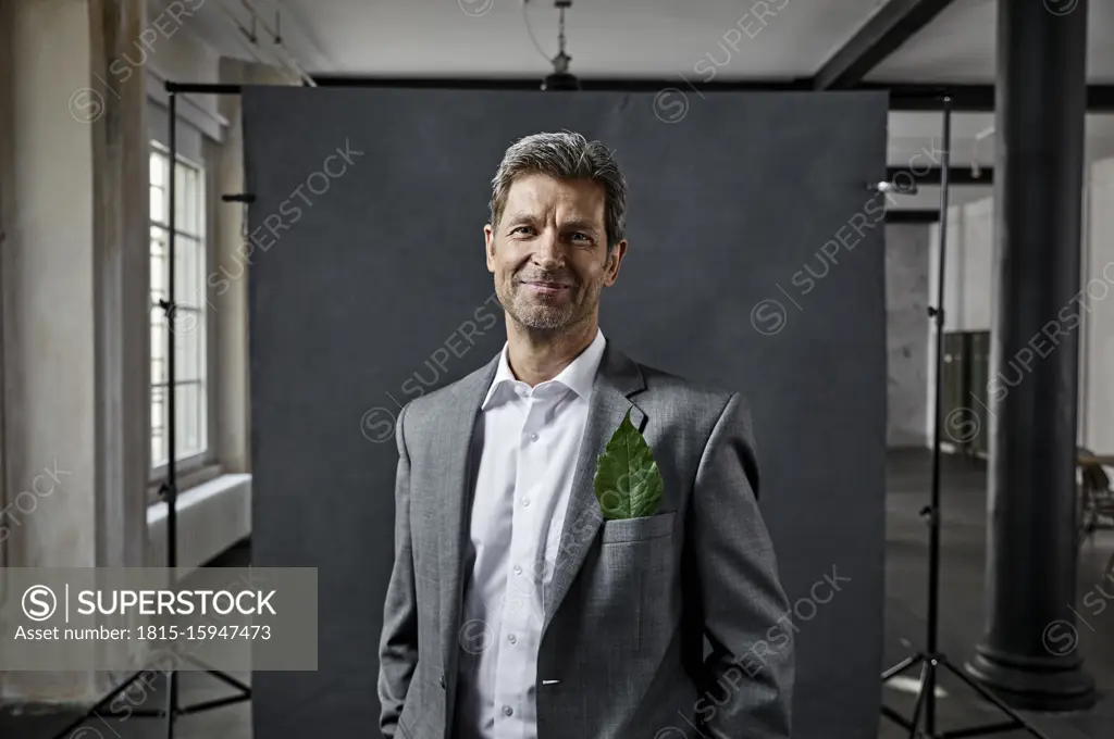 Portrait of mature businessman with leaf in pocket in front of black backdrop in loft