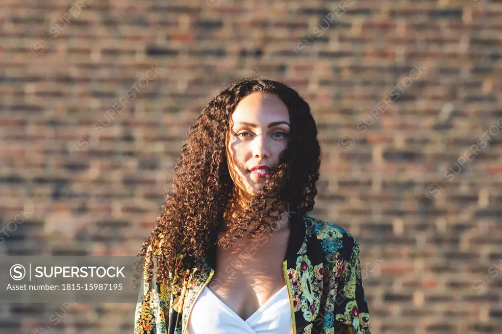 Portrait of young woman with curly hair in front of brick wall