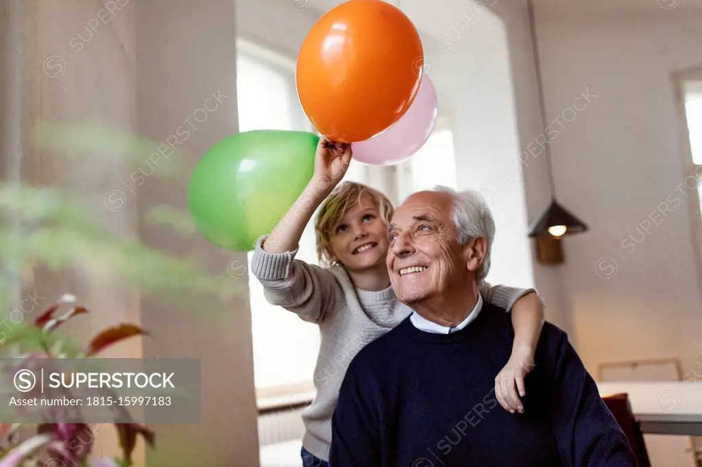 Happy grandfather and grandson playing with balloons at home