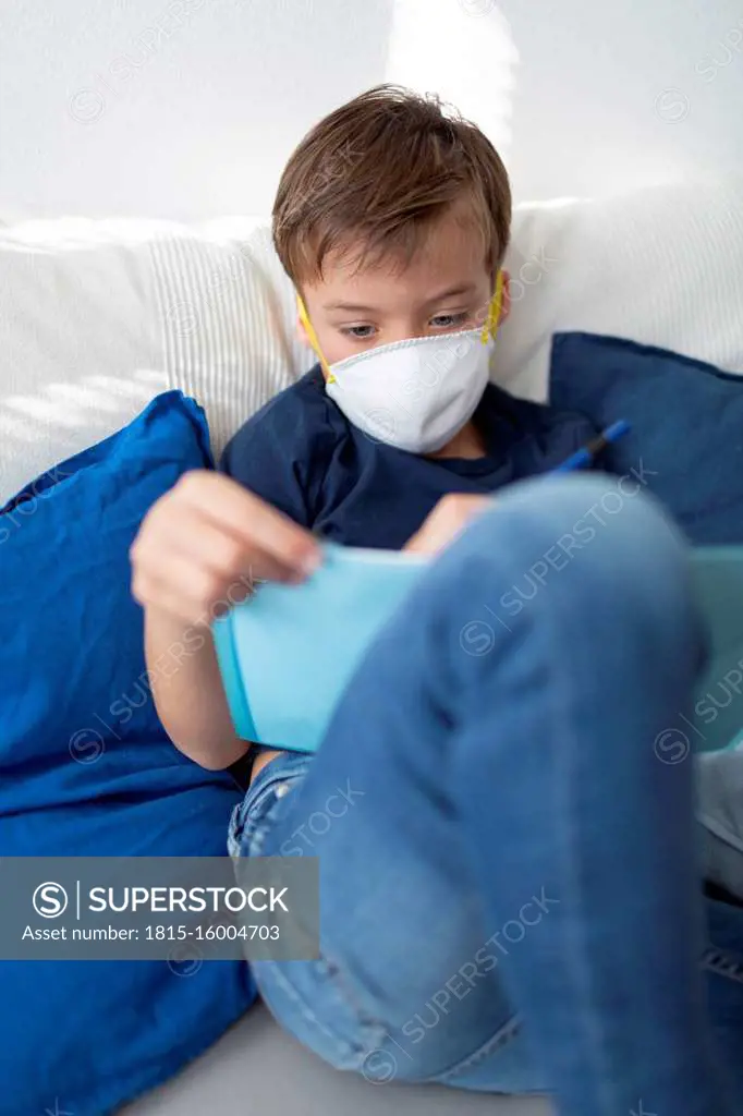 Boy with mask is in his room doing homework at home during the corona crisis