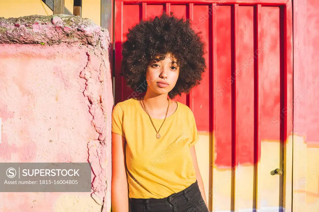 Portrait of young woman with afro hairdo leaning against a wall