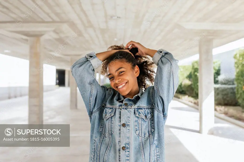 Portrait of young smiling woman pulling her hair up in parking