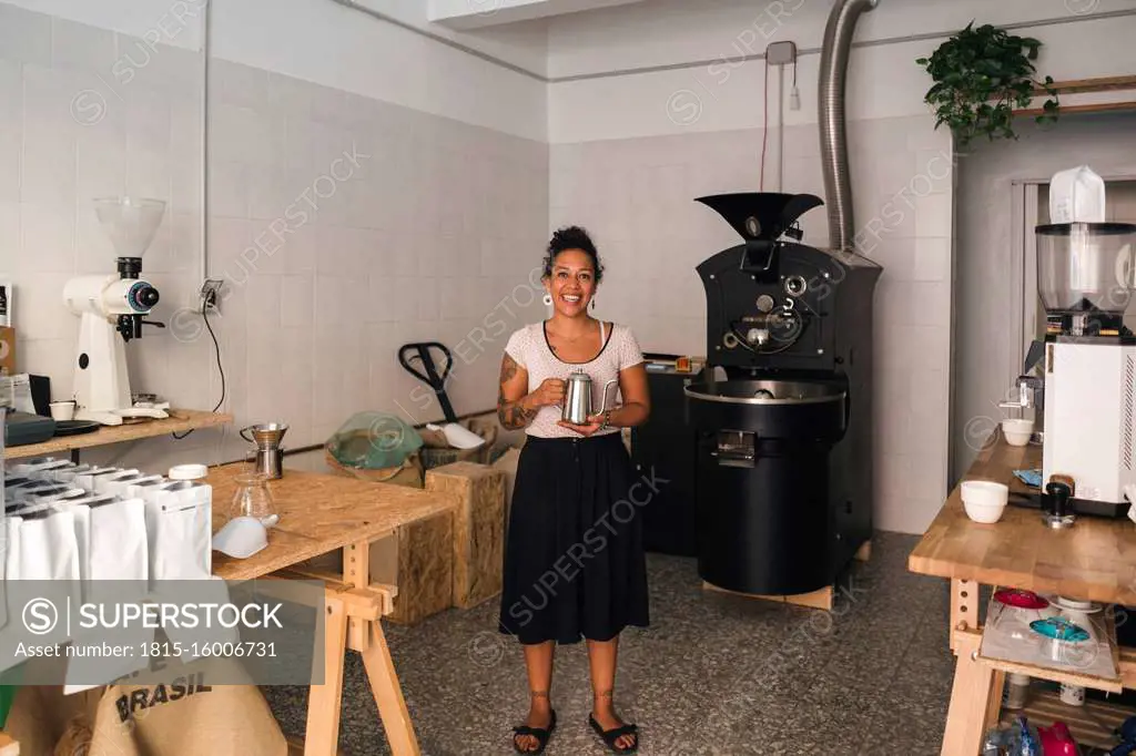 Portrait of smiling woman in a coffee roastery holding coffee pot