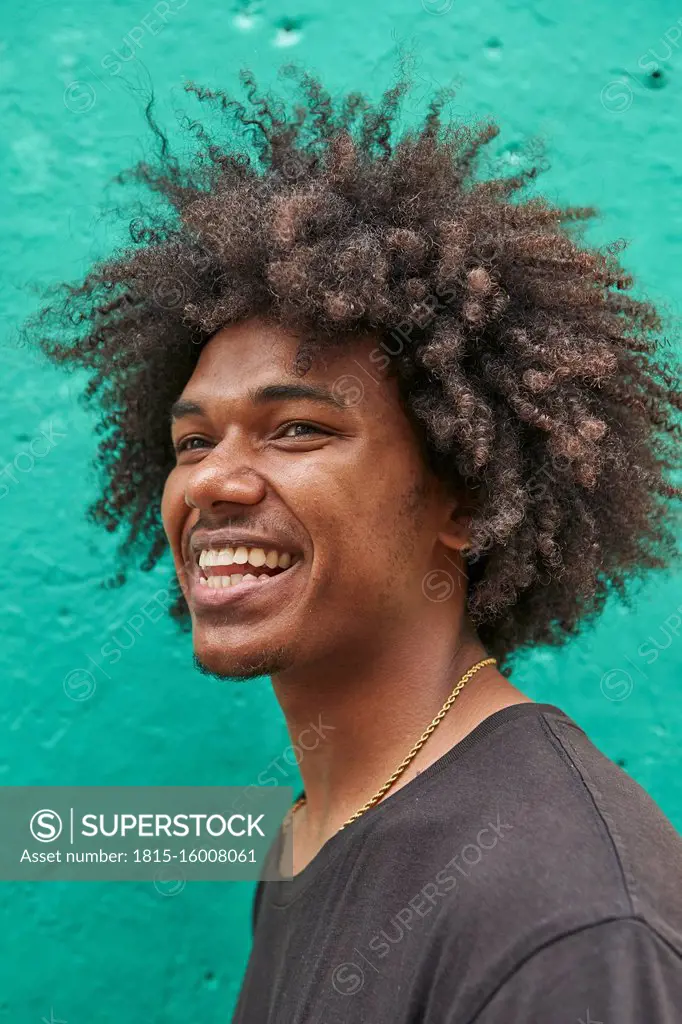 Portrait of laughing young man with afro against green wall
