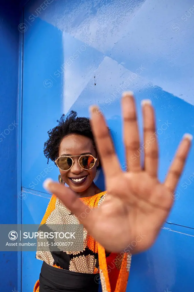 Portrait of smiling woman raising her hand in front of blue background