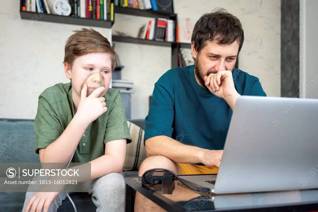 Portrait of father and son sitting together on the couch using laptop