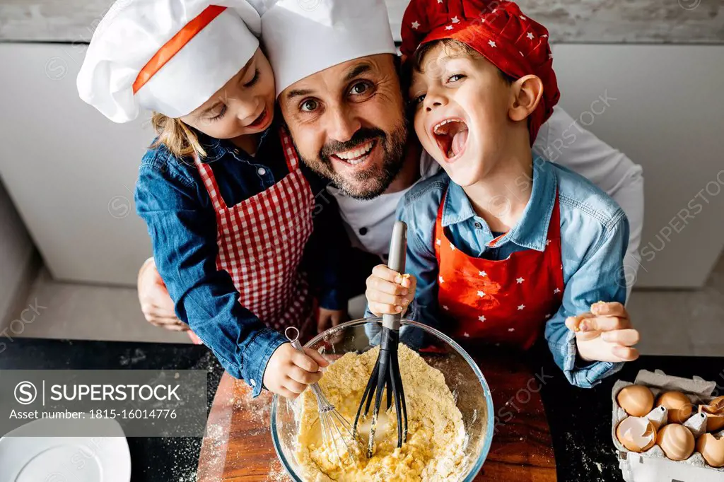 Portrait of happy father with two kids preparing dough in kitchen at home