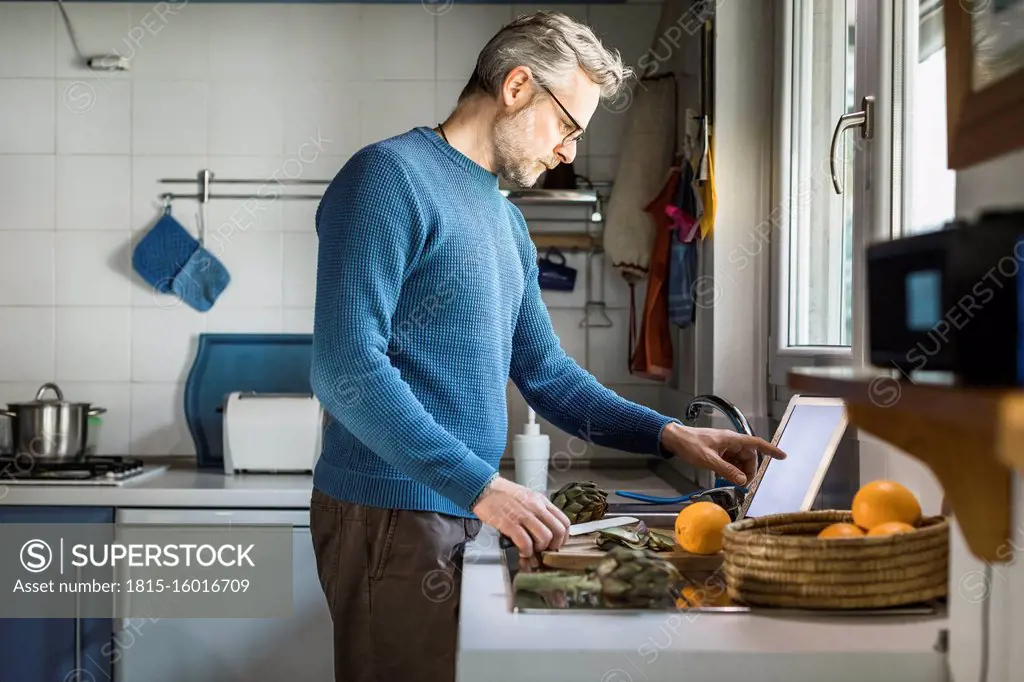 Mature man preparing artichokes in his kitchen using digital tablet