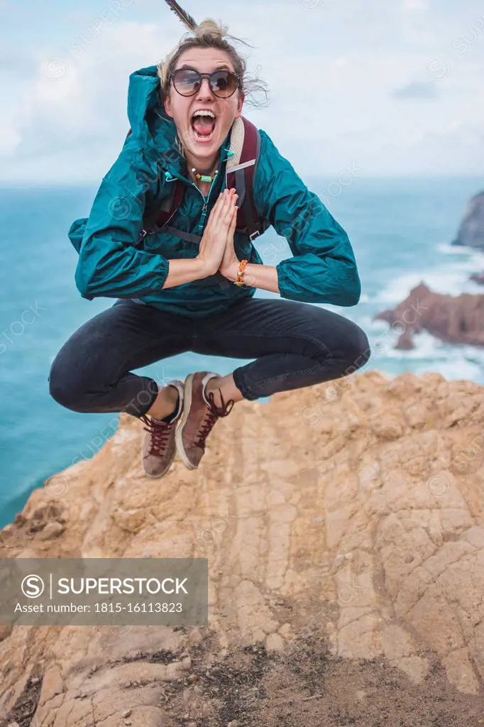 Portugal, Lisbon District, Sintra, Portrait of female hiker jumping at edge of Cabo da Roca cliff