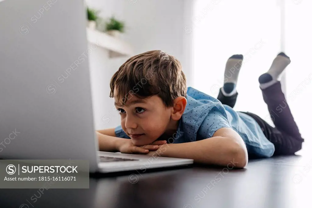 Boy lying on desk looking at laptop