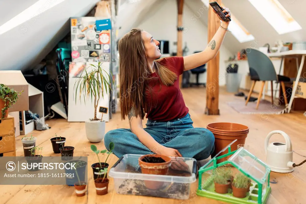 Young woman taking selfie with plants on wooden floor