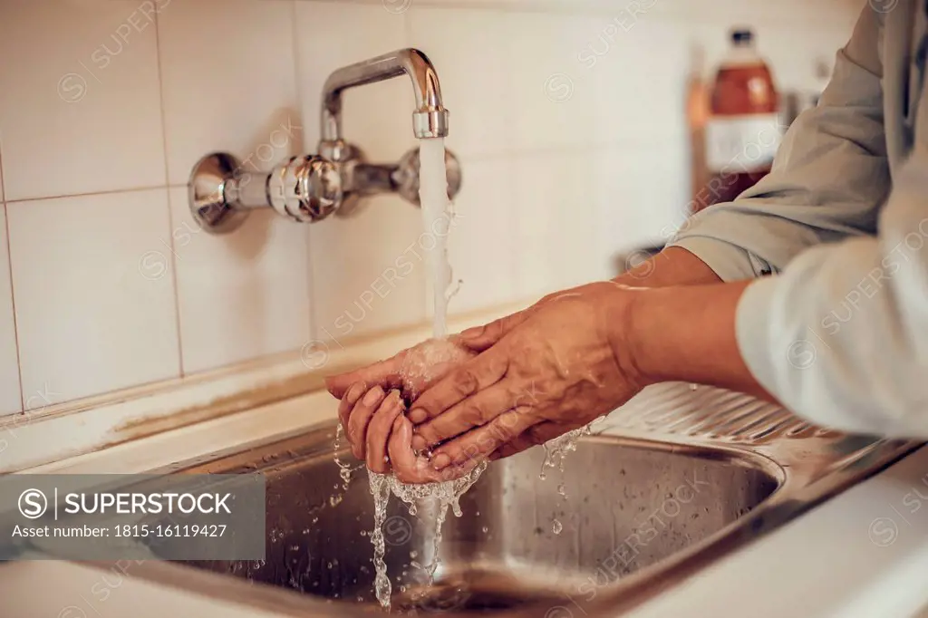 Close-up of a woman washing her hands with soap and water at the kitchen basin