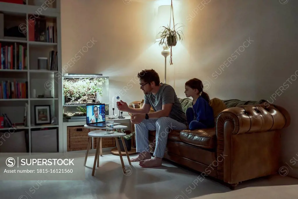 Sick girl sitting by father discussing telemedicine with doctor over video call through laptop in living room at home