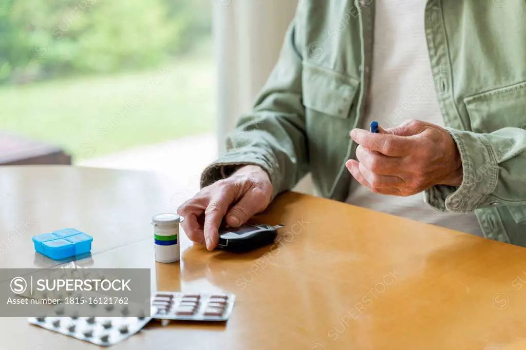 Midsection of retired diabetic senior man examining himself while sitting at table