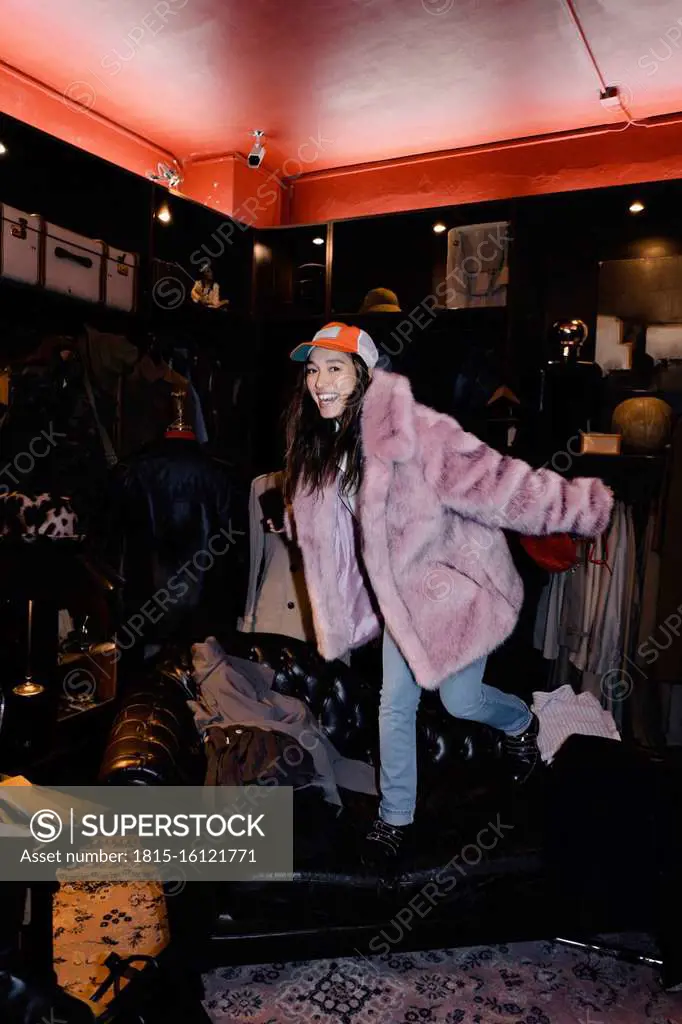 Cheerful woman wearing fur jacket standing on sofa at thrift store