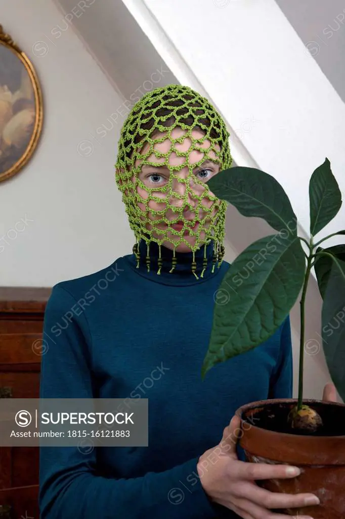 Portrait of teenage girl wearing crocheted green headdress holding potted avocado plant