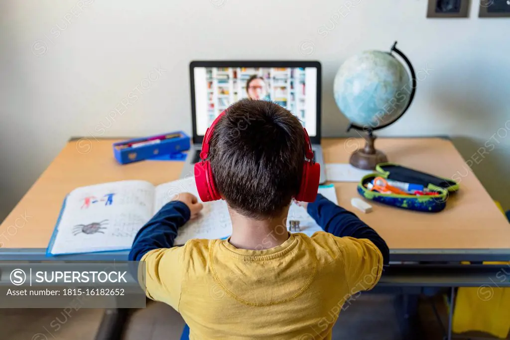 Rear view of boy listening to teacher through video call at home during pandemic outbreak