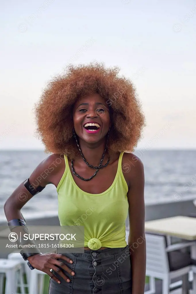 Portrait of laughing woman with afro hairstyle standing in front of the sea