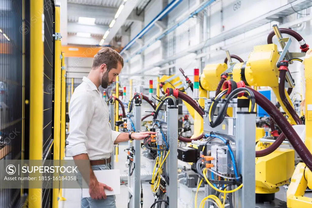 Young male engineer looking at machinery's robotic arm in automated factory